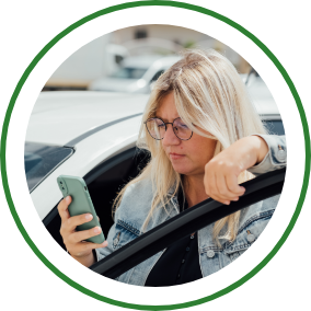 A woman stands near the open door of her vehicle and uses her smartphone.